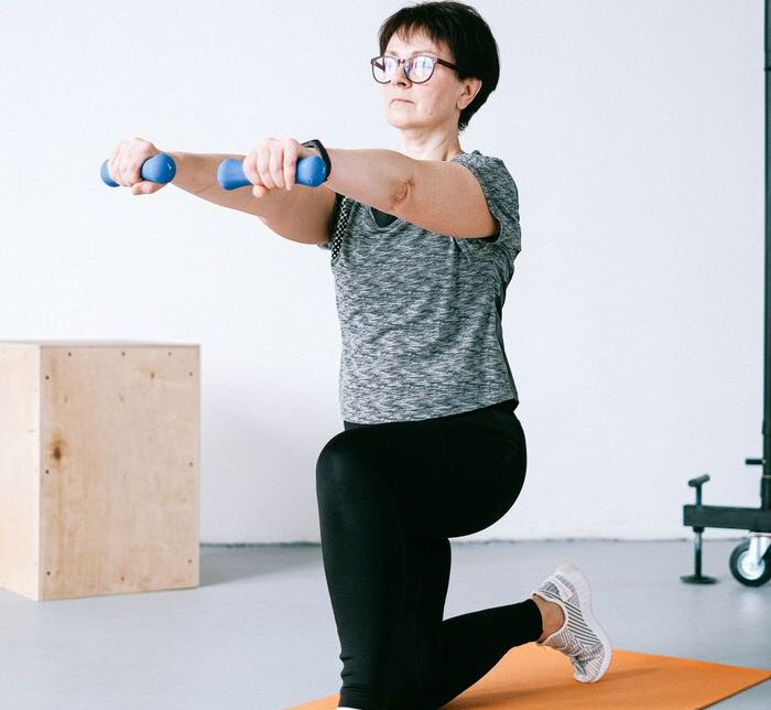Adult woman exercising indoors with dumbbells on an orange mat for a healthy lifestyle.