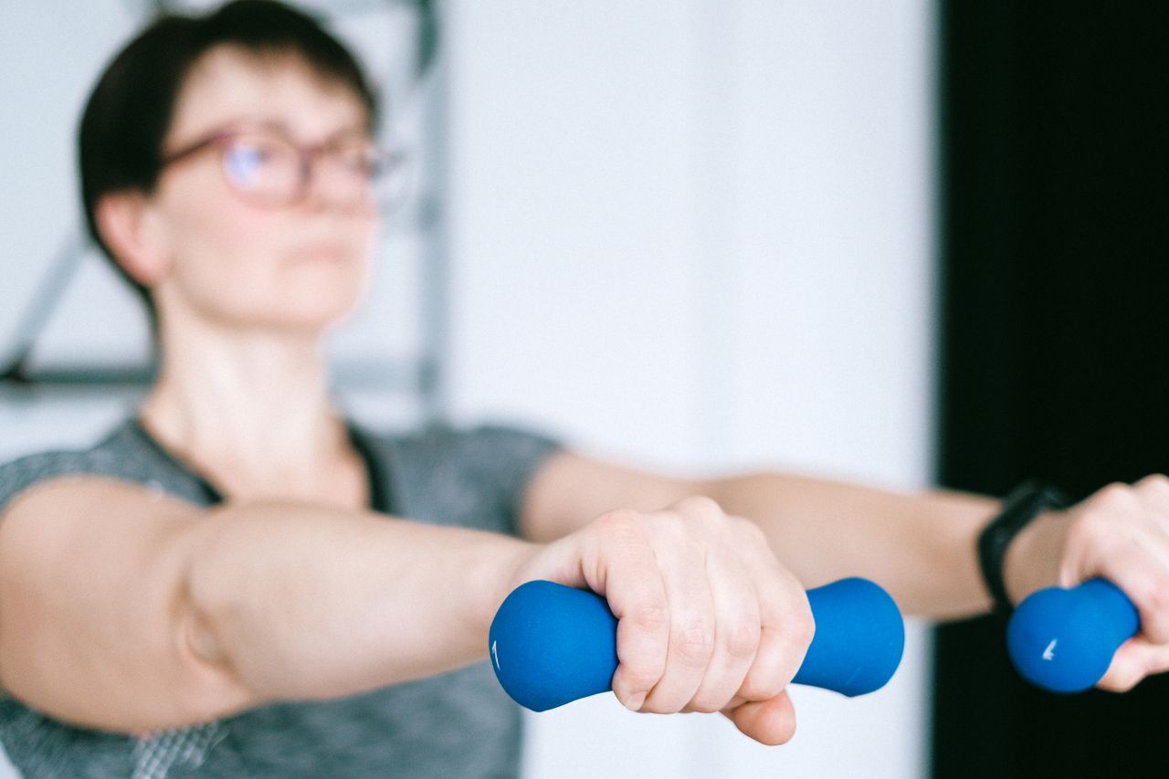 Focused woman exercising indoors with blue dumbbells, promoting a healthy lifestyle.
